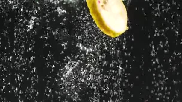 Färska citronskivor faller i vattnet på svart bakgrund. Citrus i vatten med bubblor. Ekologisk mat, hälsosam livsstil. Slow motion. — Stockvideo