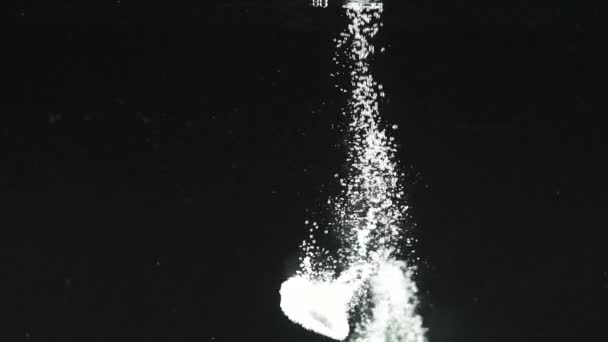 Zwei Pillen fallen in Wasser isoliert auf schwarzem Hintergrund. Effektive Auflösung von Tabletten in Wasser. Blasen steigen auf. — Stockvideo