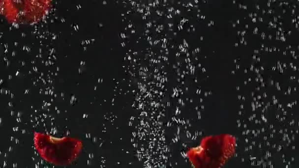 Jordgubbs halvor faller i vattnet med bubblor på svart bakgrund. Färska bär i vattnet. Ekologisk bär, frukt, hälsosam mat. Slow motion. — Stockvideo