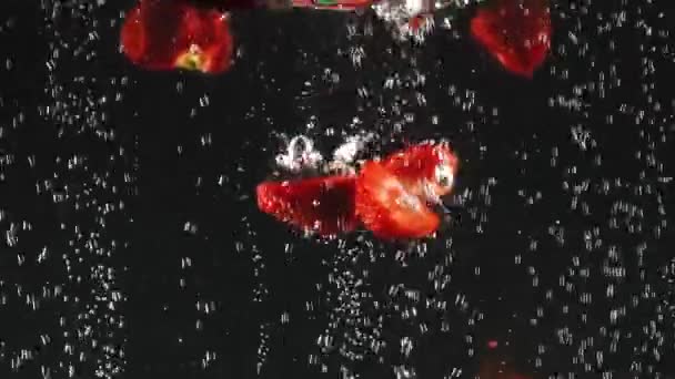 Erdbeerhälften fallen in klares Wasser auf schwarzem Hintergrund. frische Beeren im Wasser. Bio-Beeren, gesunde Ernährung. — Stockvideo