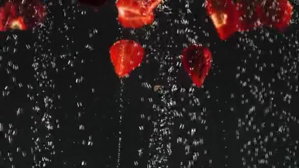 Fallende frische rote Erdbeerscheiben, die in glitzerndes Wasser auf schwarzem Hintergrund spritzen. Nahaufnahme — Stockvideo