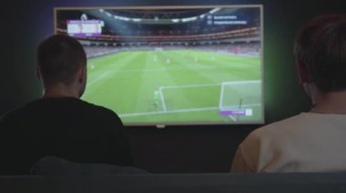 Oyun odasında video oyunu oynayan iki adam kapalı kanepede oturuyor. Arkadaşlar futbol oynuyor. Arkadaşlar birlikte vakit geçiriyor. Video oyunu ve eğlence konsepti.