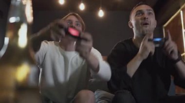 Yakışıklı genç arkadaşlar modern loft kulübünde mükemmel bir ruh hali ile bira içme video oyunları oynarken akşam eğleniyor. Video oyunu ve eğlence konsepti.