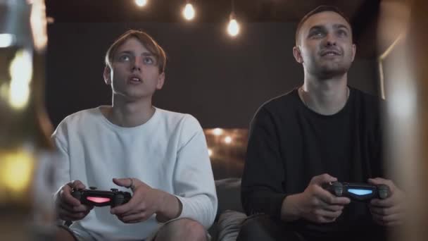 Portré két fickó játszik videojáték a játékterem ül a kanapén. Barátok harcok segítségével joystick. Barátok kiadási időt együtt bent. Videojáték-és szabadidő koncepció. — Stock videók