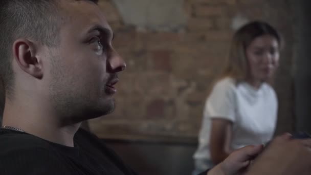 Close-up retrato chateado jovem jogando o jogo de vídeo sentado no sofá na sala de estilo loft com menina bonito. Conceito de jogo de vídeo e lazer . — Vídeo de Stock