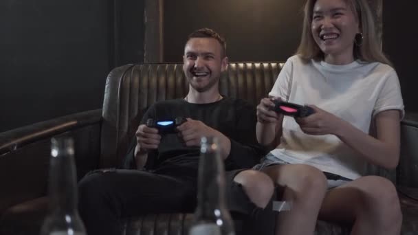 Guapo chico joven con su novia divirtiéndose jugando videojuegos bebiendo cerveza con excelente estado de ánimo en el club loft moderno. Videojuego y concepto de ocio . — Vídeo de stock