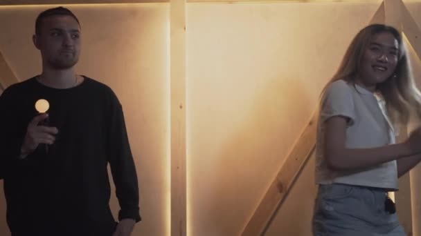 Joven hombre y mujer bailando en la habitación de estilo loft sosteniendo sensores de movimiento luminosos y sonriendo. Una pareja feliz pasando tiempo juntos. Ocio interior — Vídeos de Stock