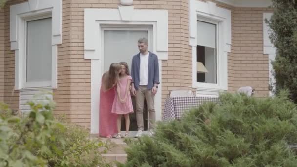 Familia feliz de pie en el porche juntos. Mamá y papá se despiden de su hijita y ella se va de casa. Tiempo libre de verano — Vídeos de Stock