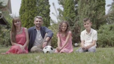 Mutlu bir aile bahçede çimenlerin üzerinde birlikte oturuyorlar. Anne, baba, oğul ve kızı kameraya gülümseyerek bakıyor. Yaz eğlencesi, kaygısız çocukluk