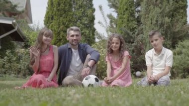 Mutlu bir aile bahçede çimenlerin üzerinde birlikte oturuyorlar. Anne, baba, oğul ve kızı kameraya bakarak gülümseyerek el sallıyor. Yaz eğlencesi, kaygısız çocukluk