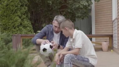 Verandada oturan baba ve oğlunun portresi elinde sönmüş bir futbol topu tutuyor. Aile birlikte vakit geçiriyor. Yaz tatili