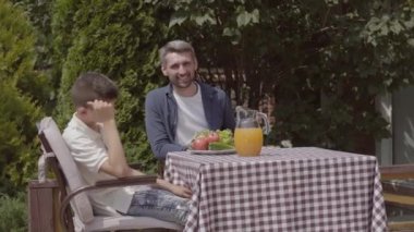 Kadın ve kız pasta getiriyorlar. Baba, anne ve iki çocukları bir masada oturup bahçede güneşli bir günün tadını çıkarırken öğle yemeği yiyorlardı. Yaz mevsimi, mutlu aile