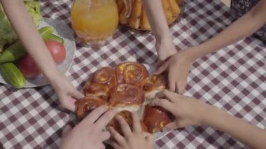 Taze pişmiş kek sebze ve meyve suyu kavanozu yakınında masada yatıyor. Tanınmayan insanların elleri aynı anda taze hamur işi parçaları alıyor. Mutlu dost aile kahvaltısı.