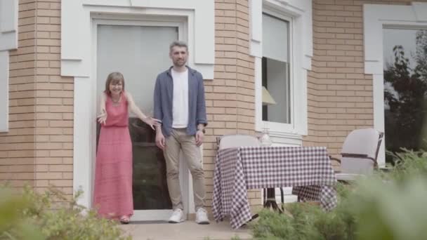 Gelukkige familie staan samen op de veranda. Moeder en vader begroette dochter die met vrienden in de buurt van het huis speelde, het kind knuffelen ouders. Zomer vakantie — Stockvideo