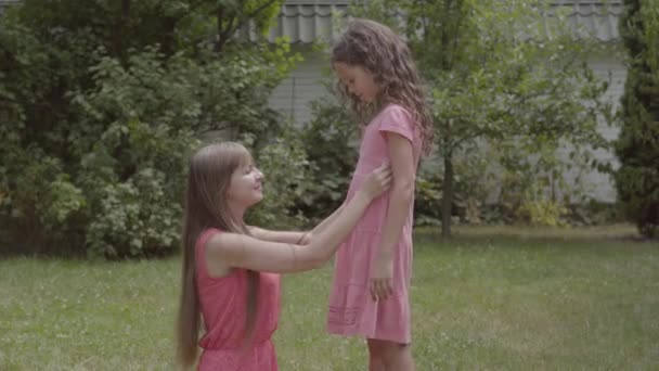 Jeune belle femme aux cheveux longs assise sur l'herbe et caressant sa fille dans le jardin. La famille passe du temps ensemble. Loisirs d'été — Video