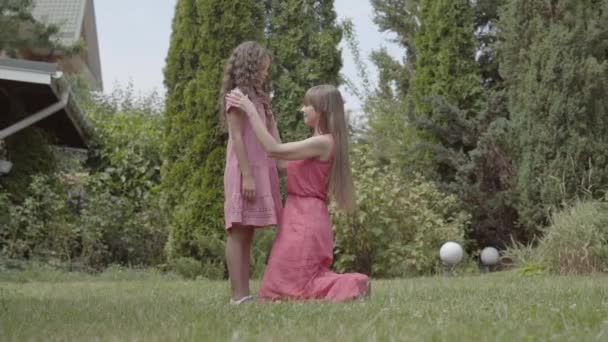 Молода красива жінка з довгим волоссям сидить на траві зі своєю дочкою в саду. Сім'я проводить час разом. Літній відпочинок . — стокове відео