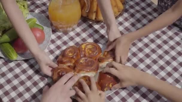 Freshly baked cakes lying on the table near vegetables and juice jar. Hands of unrecognized people taking pieces of fresh pastry at the same time. Breakfast of happy friendly family. — Stock Video