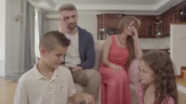 Erkek ve kız kardeş ön planda tartışırken, kafası karışık anne ve baba arka planda kanepede oturuyor. Yaramaz çocuklar, çocuk yetiştirmede zorluklar