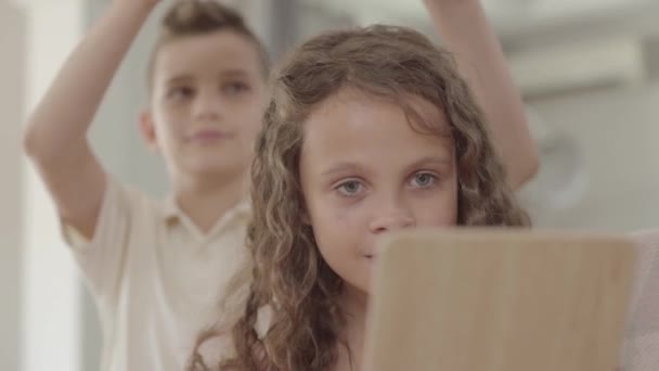 The boy putting the crown on the head of curly girl looking in the mirror. The crown is too big for the child, kids laughing. Gallant boy caring for a beautiful girl — Stock Video