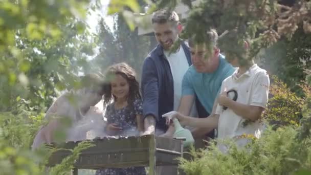 Feliz familia amistosa haciendo barbacoa en el primer plano del jardín. Tiempo libre de verano. Gente cocinando carne en la parrilla al aire libre — Vídeos de Stock