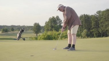 Golf sahasında tek başına golf oynayan sevimli yaşlı adam. Kıdemli adam golf sopasını kullanarak topa vurdu. Adam yumruk atıyor ve topa vuruyor. Yaz eğlencesi. Zafer kavramı