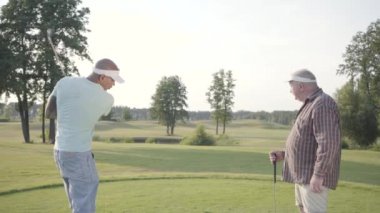 Kendine güvenen orta doğu golfçü sallanan ve güzel bir ders golf topu isabet. Yaşlı bir adam rakibini izler ve beş verir. Rekreasyon ve spor açık havada kavramı.