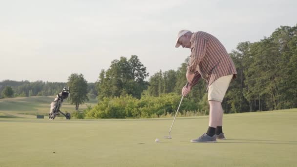 Зрілий чоловік грає в гольф сам на полі для гольфу. Старший чоловік вдарив м'яч за допомогою гольф-клубу. Хлопець робить удар і кидає м'яч. Літнє дозвілля. концепція Перемоги — стокове відео