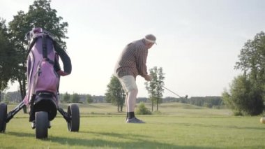 Golf sahasında golf oynayan olgun adam. Kıdemli adam golf sopasını kullanarak topa vurdu. Yaşlı beyefendi dışarıda oyun oynuyor. Yaz eğlence