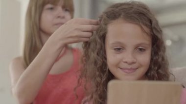 Güzel genç anne aynaya bakarak onu sevimli kızı örgüler. Aile ilişkileri.