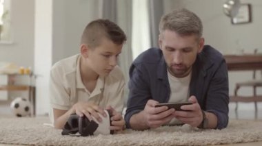 Baba ve oğlu sanal gerçeklik gözlükkullanarak kabarık halı üzerinde yerde yatan, evde mutlu dostu aile. İlişki baba ve oğul.