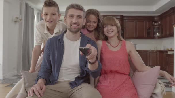 Portrait heureux adorable famille regarder la télévision à la maison ensemble. Le père tient la télécommande et change de chaîne, la femme est assise à côté de son mari et deux enfants sont avec leurs parents. Famille — Video