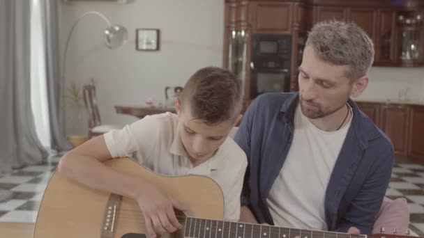 Far lär sonen att spela gitarr hemma. Familjens fritid uppfostran. Relationen far och son. — Stockvideo