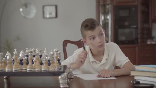 Retrato de adorable tipo considerado sentado en la mesa en casa. El chico amaneció y escribió algo en un pedazo de papel. . — Vídeos de Stock