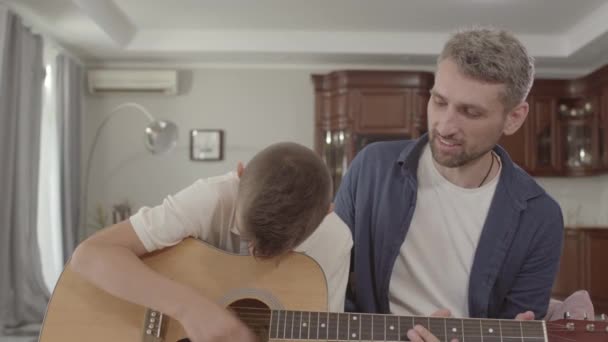 Father teaches son to play guitar at home. Family Leisure Upbringing. Relationship father and son. — Stock Video