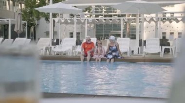 Küçük torunu ile lüks havuzun kenarında oturan Eğlenceli mutlu olgun çift. Büyükanne, büyükbaba ve torun sohbet. Mutlu dost bir aile. Otelde dinlenin. Rekreasyon ve eğlence