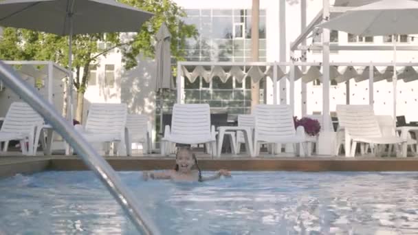 Pequena menina bonito nada em uma bela piscina em um resort caro. Recreação e lazer ao ar livre . — Vídeo de Stock