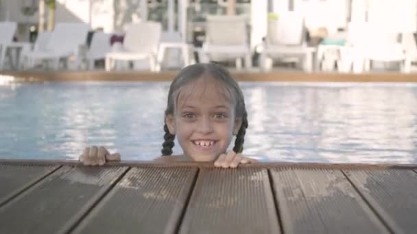 Linda chica divertida en gafas de sol amarillas mirando en la cámara sonriendo, mirando fuera de la piscina, aferrándose al borde. Niño divirtiéndose en el complejo hotelero. Recreación y ocio al aire libre . — Vídeo de stock