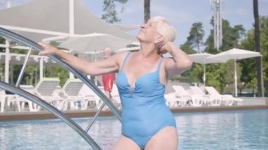 Mutlu olgun çift birlikte otel kompleksinde havuzda rahatlatıcı. Çekici yaşlı kadın güneşleniyor ve kocasına el sallıyor. Mutlu dost bir aile. Otelde dinlenin