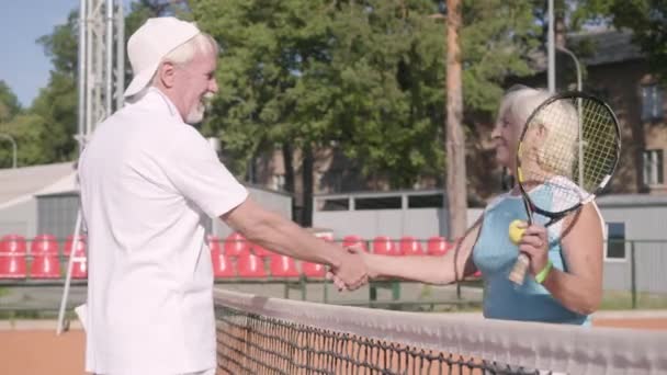 Vuxen kvinna skakar hand med stilig mogen man rival stående på en tennisbana i strålar av sommarsolen. Rekreation och fritid utomhus. — Stockvideo