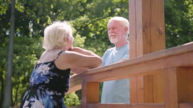 Mutlu olgun çift köprüde konuşurken ve gülümsüyor duruyor. Yaz elbisesi ve sakallı adam bir tarihte güzel yaşlı kadın. Adam bayanın saçlarını okşuyor. Romantik ilişki