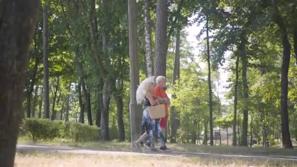 Feliz casal maduro andando no parque juntos. Mulher idosa elegante segurando guarda-sol. Velho homem e mulher passar o tempo ao ar livre, conexão com o lazer. Vista lateral — Vídeo de Stock