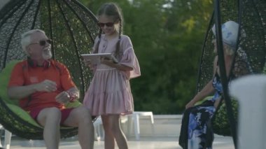 Olgun çift birlikte otel kompleksinde rahatlatıcı bir asılı sandalyede oturuyor. Sevimli küçük kız dedesi yanında duran, adam ona bir tablet veren. Otelde dinlenin. Yavaş çekim