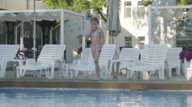 Yüzme takım elbiseli iki pigtails ile sevimli komik kız havuza atlama ve suda eğlenceli sıçrayan. Otel kompleksinde eğlenen çocuk. Açık havada eğlence ve eğlence. Yavaş çekim.