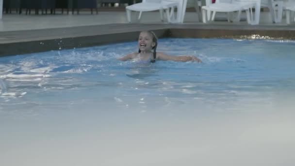 Μικρό χαριτωμένο κορίτσι κολυμπάει σε μια όμορφη πισίνα σε ένα ακριβό θέρετρο. Αναψυχή και αναψυχή σε εξωτερικούς χώρους. Αργή κίνηση. — Αρχείο Βίντεο