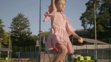 Açık havada tenis oynayan iki pigtails ile sevimli komik kız. Konsantre çocuk bir raket ve topu geçmek üzere tutuyor. Yaz tatili