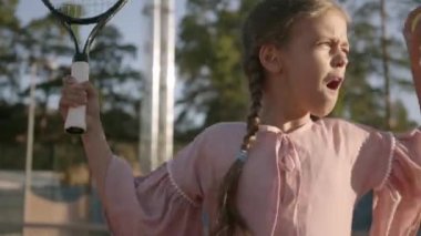 Açık havada tenis oynayan iki pigtails ile sevimli komik kız. Konsantre çocuk bir raket ve topu geçmek üzere tutuyor. Yaz tatili