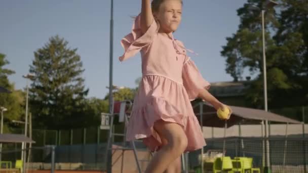 Rozkošná legrační holka se dvěma pigocky hrající tenis venku. Soustředěné dítě, které drží rámus a míč kolem. Letní čas — Stock video
