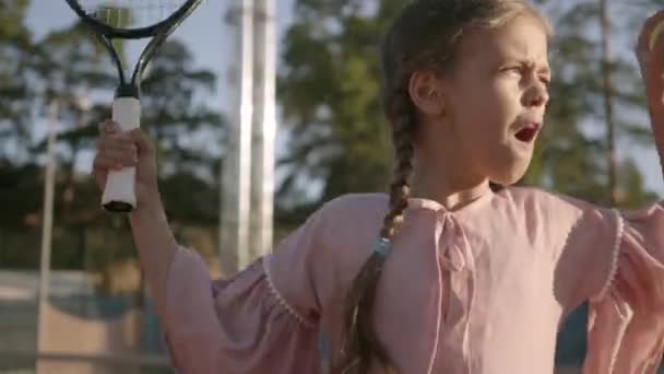 Roztomilá, zábavná holka se dvěma pigocky hrající tenis venku. Soustředěné dítě, které drží rámus a míč kolem. Letní čas — Stock video