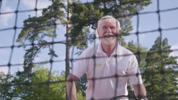 Retrato alegre feliz sonriente hombre maduro jugando tenis en la cancha de tenis. El viejo lanza la pelota con la raqueta. Recreación y ocio al aire libre . — Vídeos de Stock