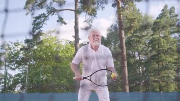 Glad lycklig leende mogen man spela tennis på tennisbanan. Den gamle mannen kastar bollen med racket. Aktiv fritid utomhus. — Stockvideo